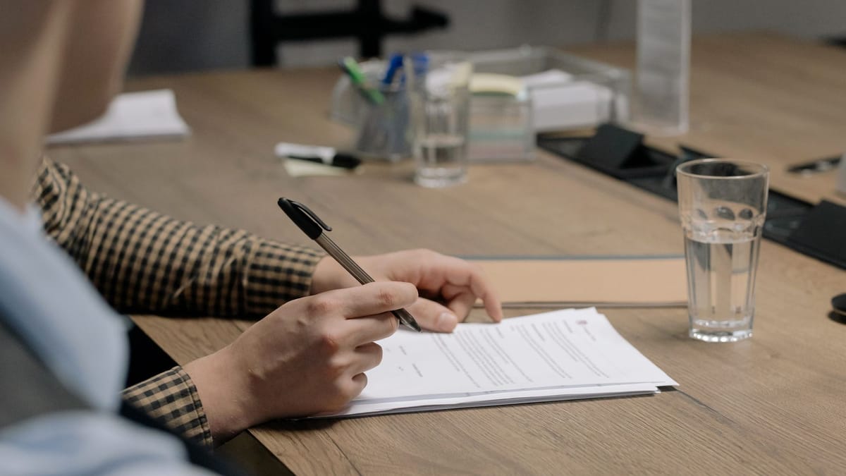 Uma mão com uma caneta sobre documentos de negócios numa mesa de escritório
